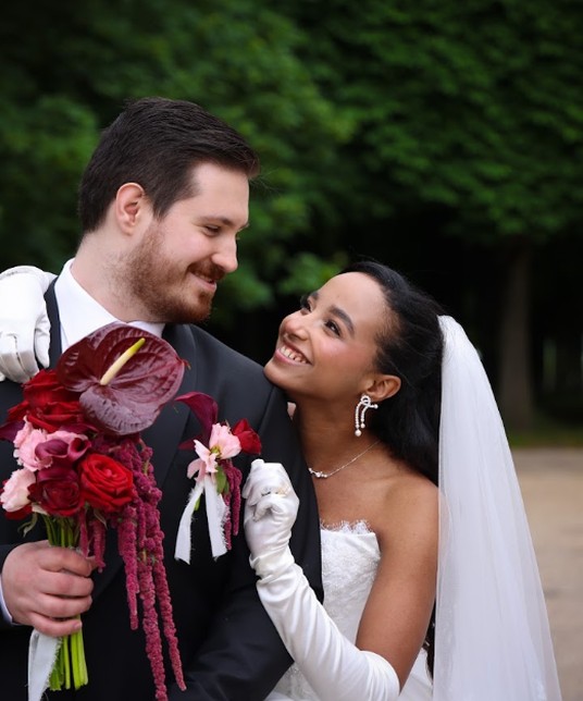 Amina and Anthony, sharing a knowing look, burgundy bouquet