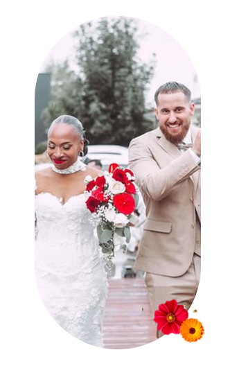 Mariée en robe de dentelle avec un bouquet rouge, au côté de son marié en costume beige