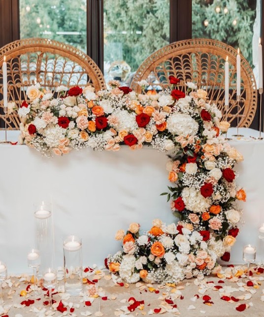 Top table with an arch of red, orange and white flowers, candles and petals